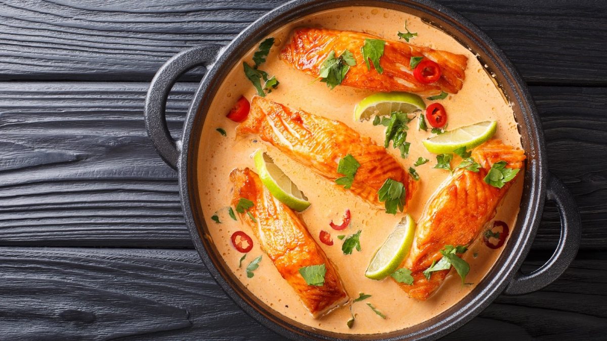 Rotes Curry mit Lachsfilet in einem schwarzen Topfauf schwarzem Hintergrund