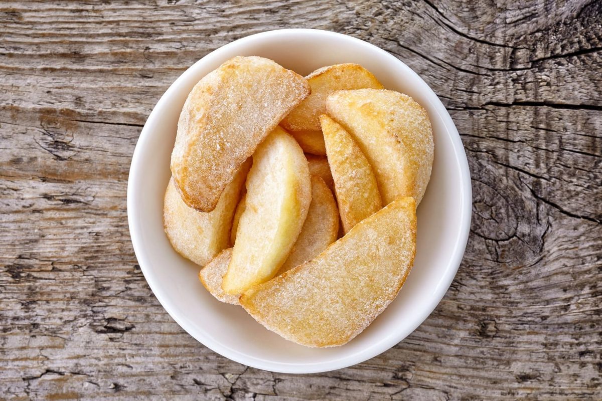 Gefrorene Kartoffeln in weißer Schüssel auf Holzplatte.