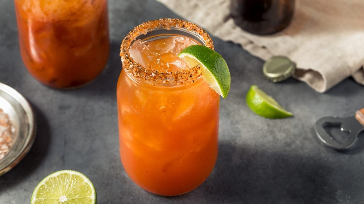 Zwei Gläser mit dem Kimchi-Bloody-Mary auf einem grauen Tisch mit Limette und Barequipment.