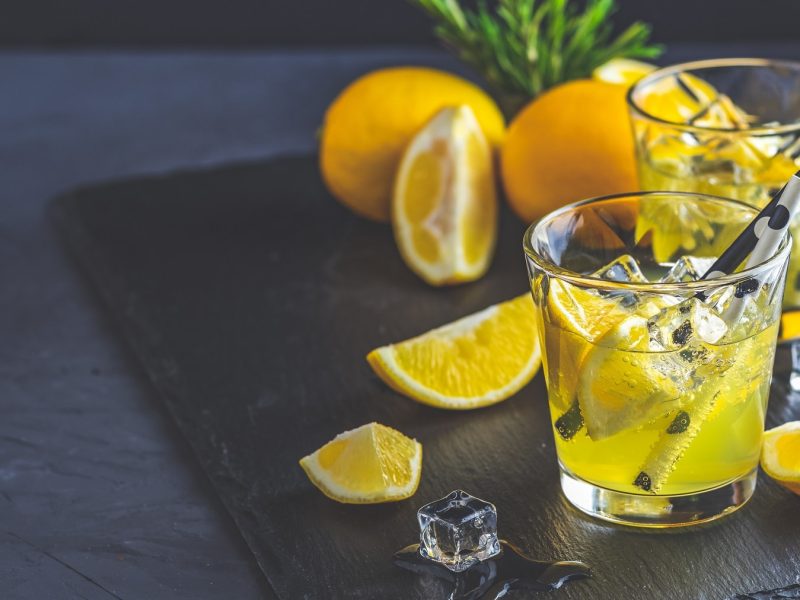 zwei Gläser Limoncello Tonic mit Eiswürfeln und Zironenstücken, darin Strohhalme. Drumherum frische angeschnittene Zitronen.