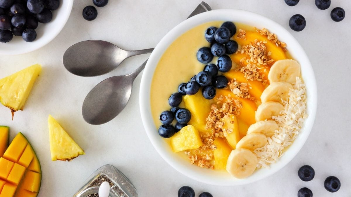 Mango-Smoothie-Bowl in einer weißen Schale neben zwei Löffeln