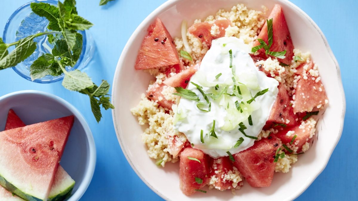 Melonensalat mit Couscous und Gurke, getoppt mit griechischem Joghurt und Minze. Draufsicht.