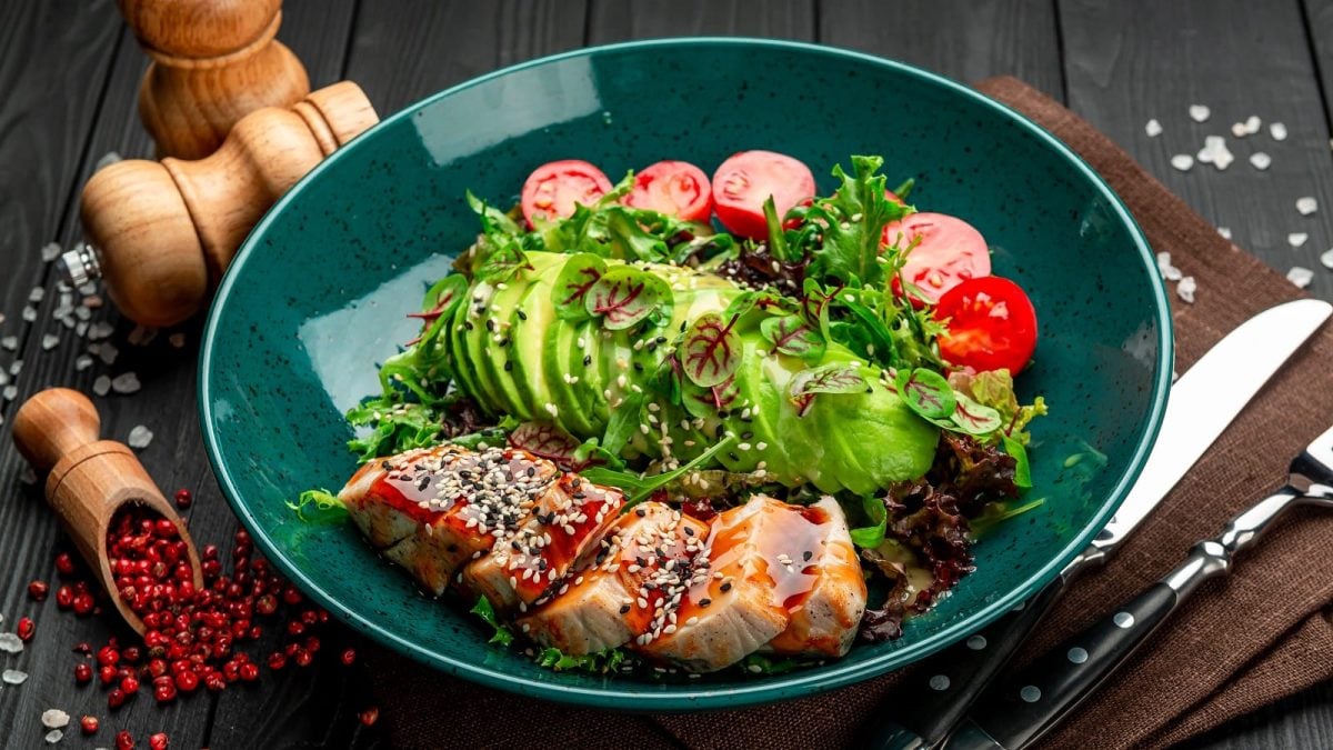 Eine blaue Schale mit Putensalat mit Teriyakisauce neben rotem Pfeffer und Besteck