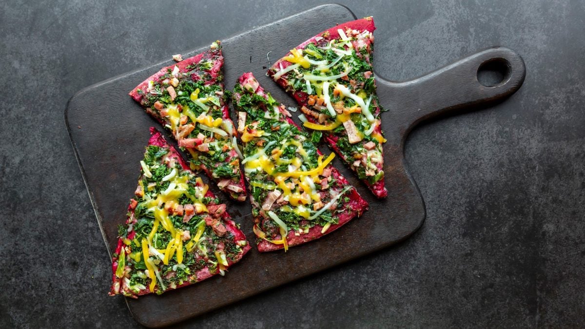 Vier Stücken der Rote-Bete-Pizza auf einem schwarzen Brett und grauem Untergrund.