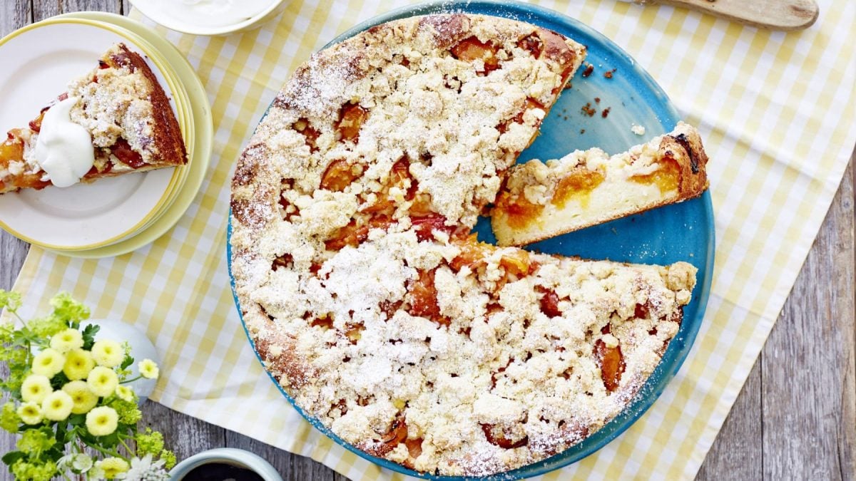 Skyr-Aprikosen-Streuselkuchen auf einem blauen Teller auf einer weißgelb karierten Tischdecke.