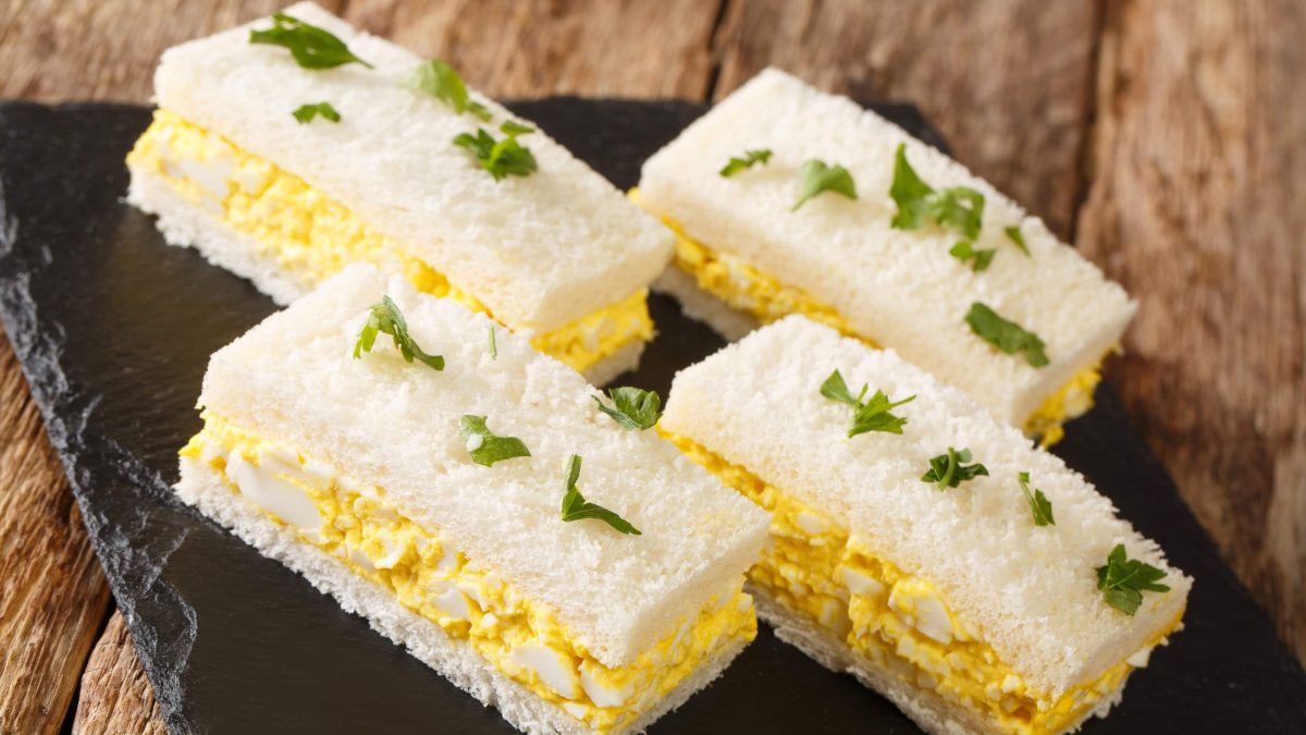 Tamago Sando japanisches Eiersalat-Sandwich mit Shiso auf Schieferplatte auf Holztisch. Draufsicht.