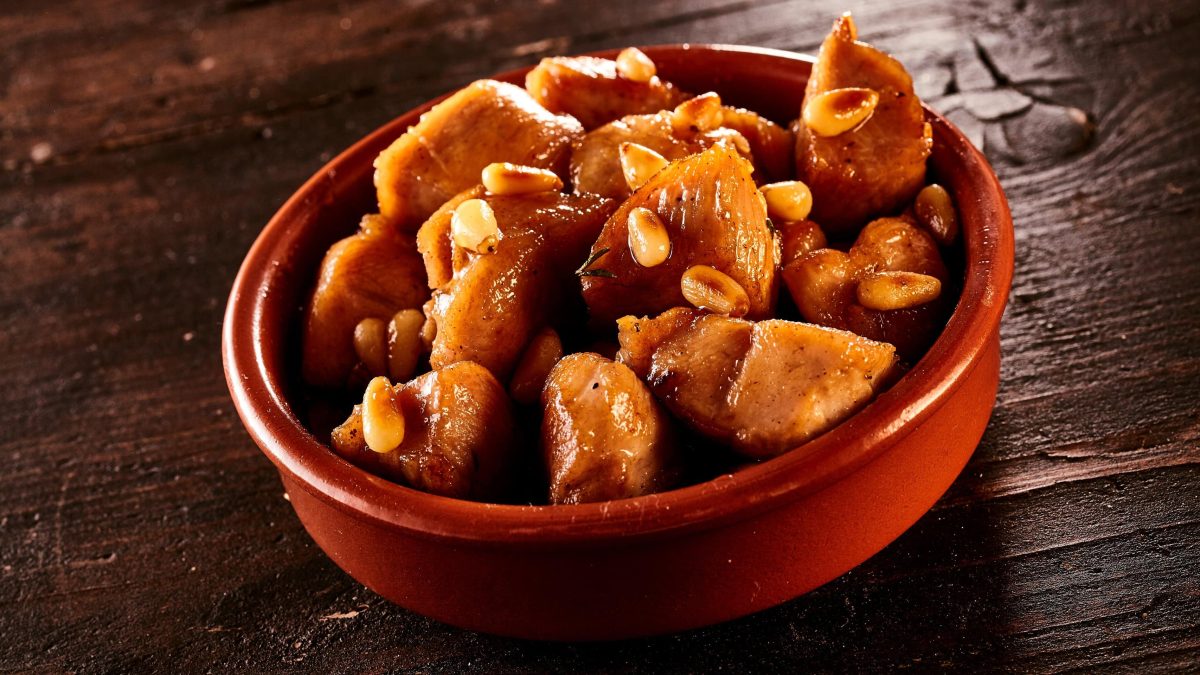 Tapas Style spanisches Honig-Hähnchen mit Pinienkernen und Portwein in Tapas-Schale auf dunklem Holz. Frontalansicht.