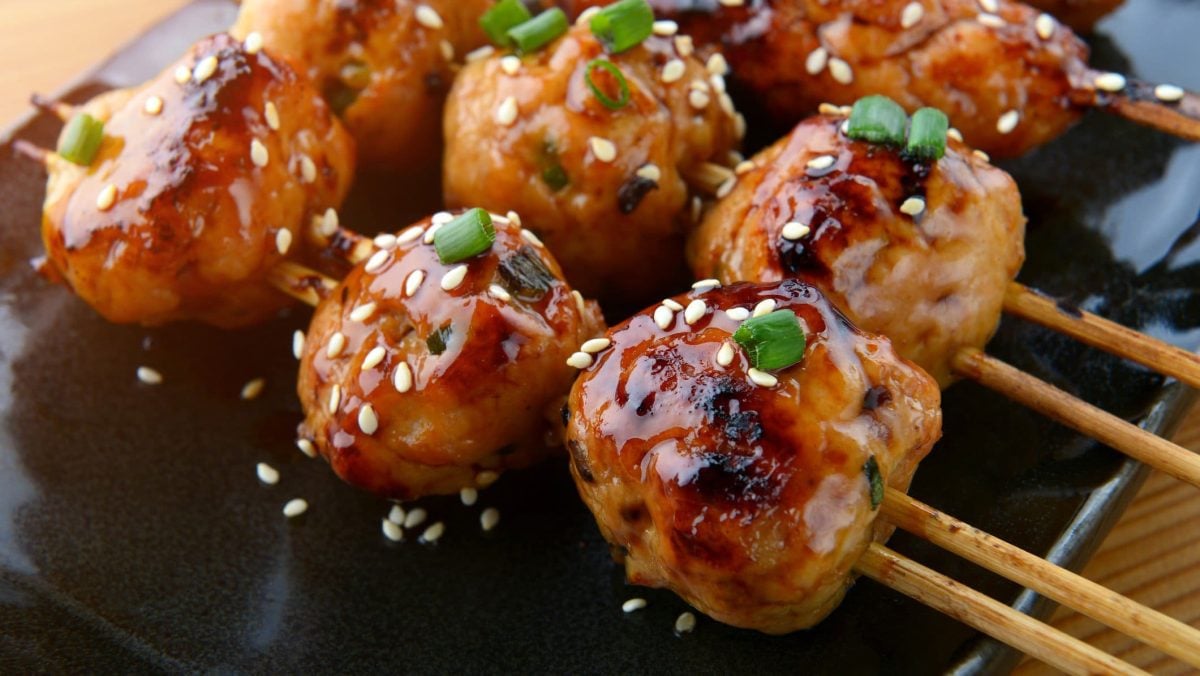 Tsukune Yakitori auf schwarzer Platte auf Holztisch. Draufsicht.