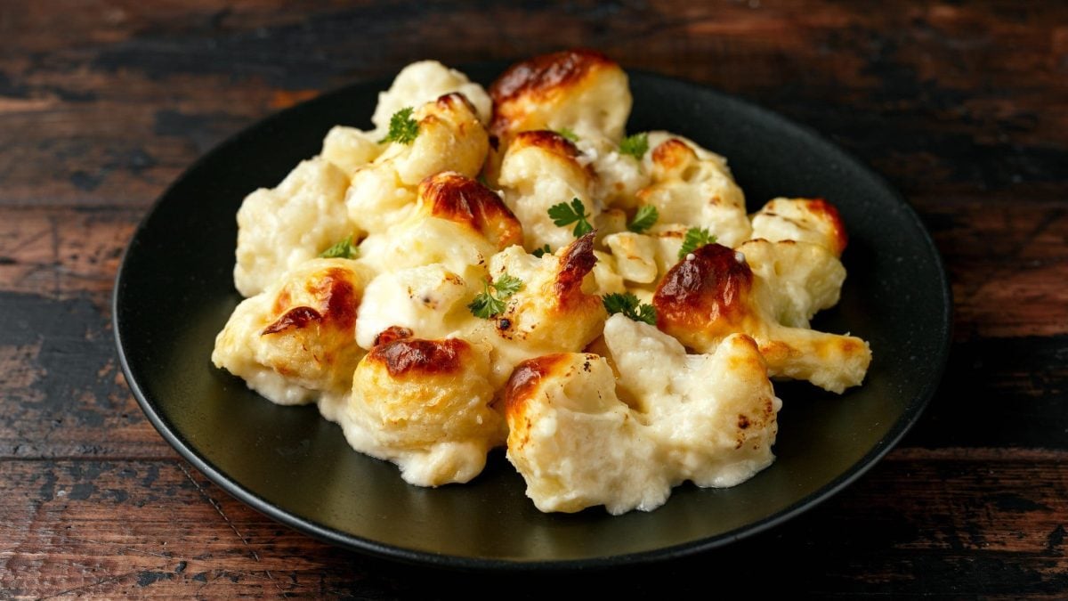 Überbackener Blumenkohl mit Käse-Sahne-Sauce auf schwarzem Teller