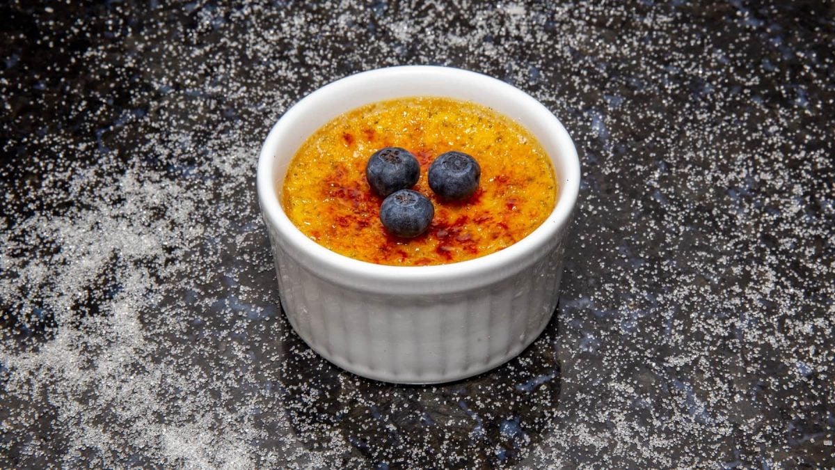 Eine kleine weiße Schale vegane Crème brûlée mit drei Heidelbeeren.