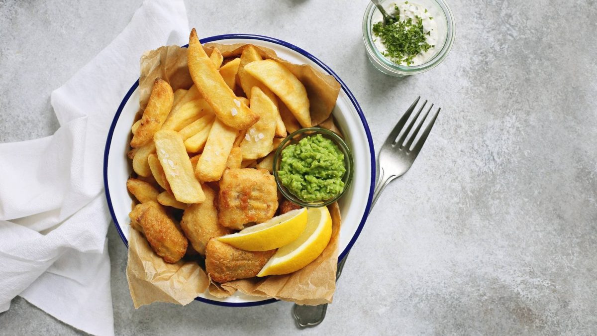 eine Schüssel vegane Fish and Chios mit Erbsenpüree, daneben eine Gabel und eine Schale mit Mayonnaise, alles in der Draufsicht.