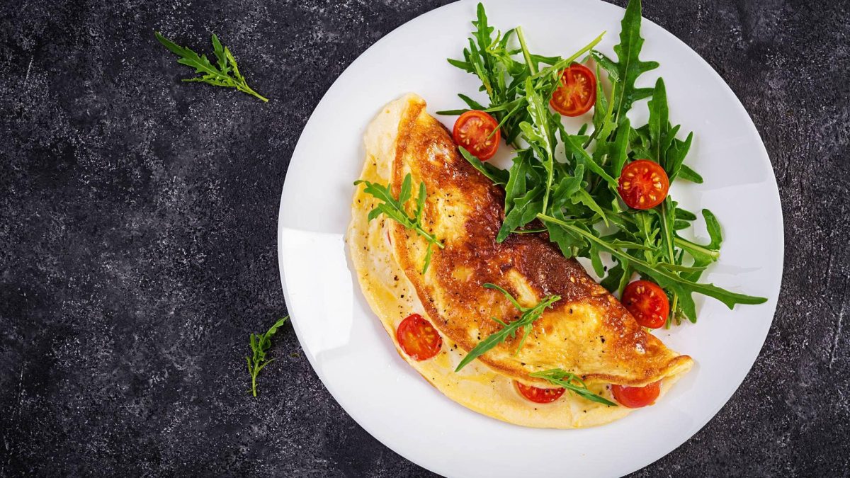 Ein veganes Omelett mit Tomaten und Rucola auf einem Teller in der Draufsicht.
