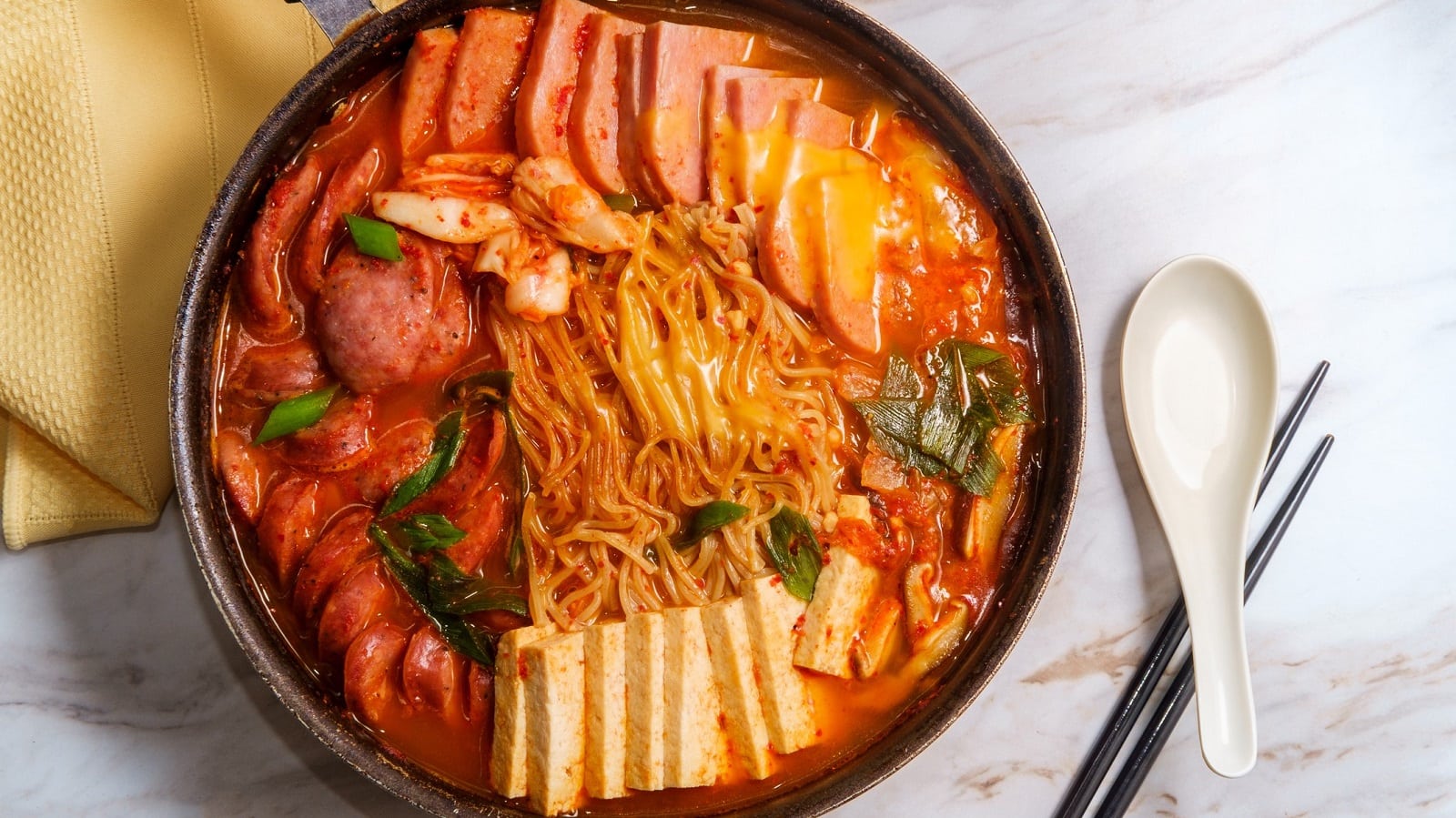 Ein Topf mit Budae jjigae neben Besteck.