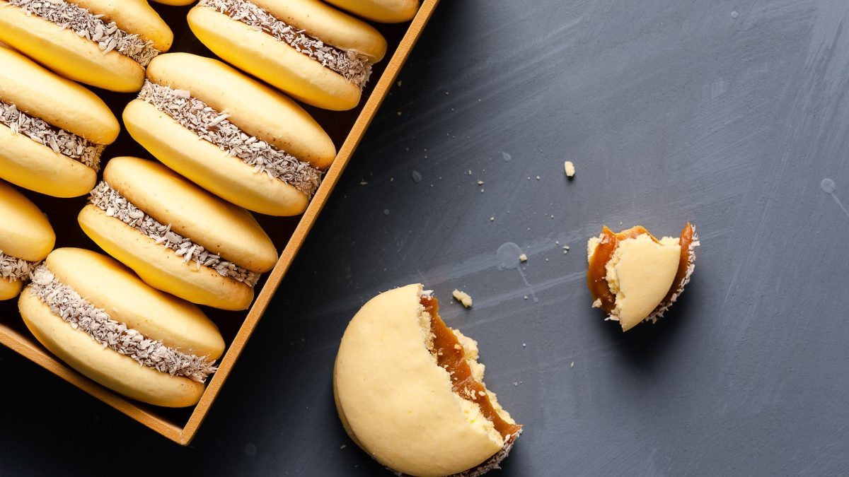 Box mit mehreren Alfajores, daneben ein einzelner in zwei Stücken vor dunklem Hintergrund.