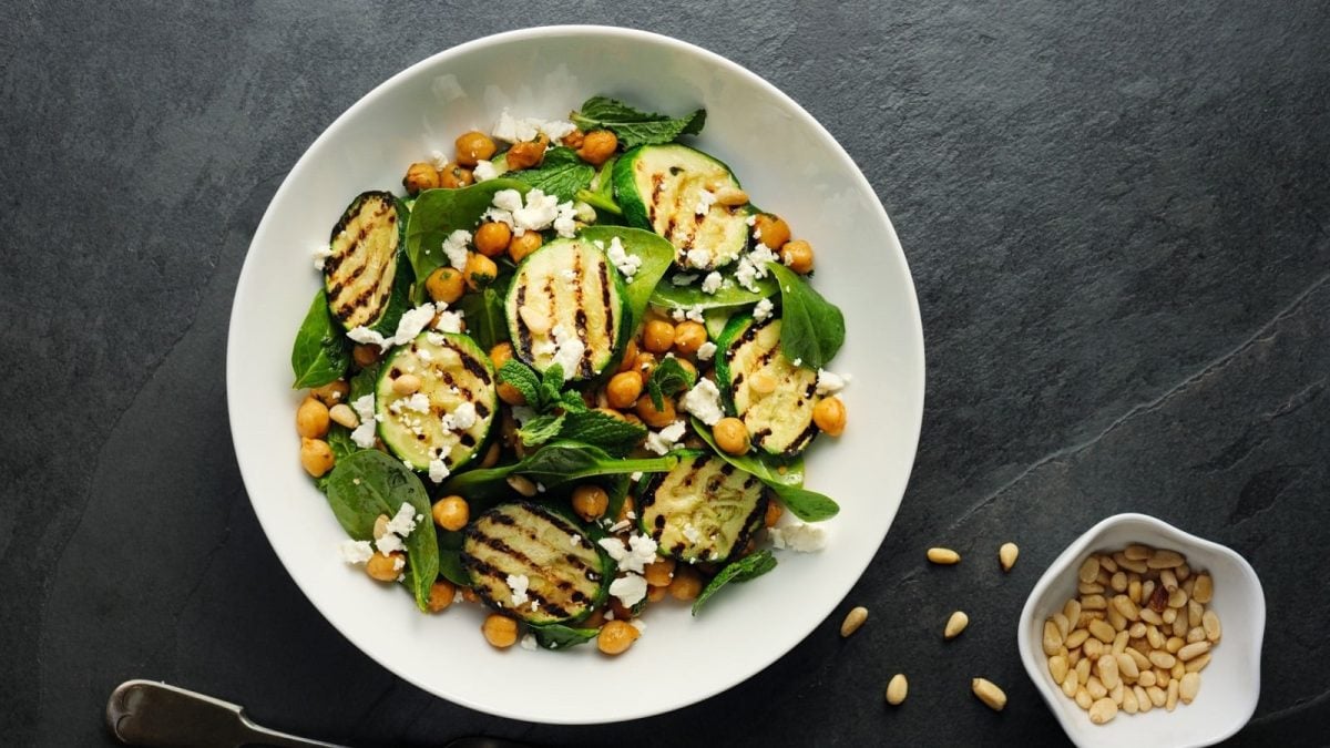 Ein weißer Teller mit gegrillter Zucchini mit Kichererbsen und Feta.