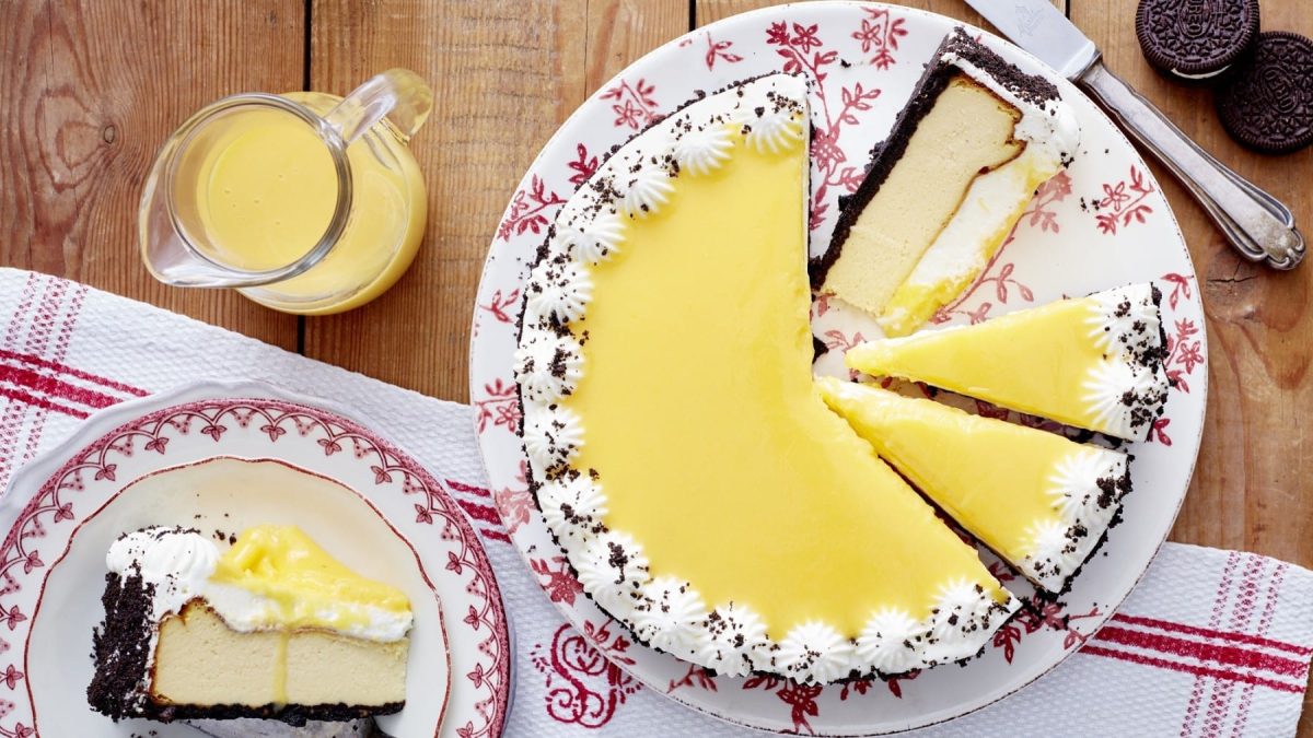 Kakaokeks-Käsekuchen, bestehend aus einer Eierlikörkäsekuchencreme, einem Kakaokeksboden und einer Garnitur aus kleinen Sahnetupfern und Eierlikörglasur, serviert auf einem rot-weißen Teller mit Blumenmuster auf einem Holztisch.