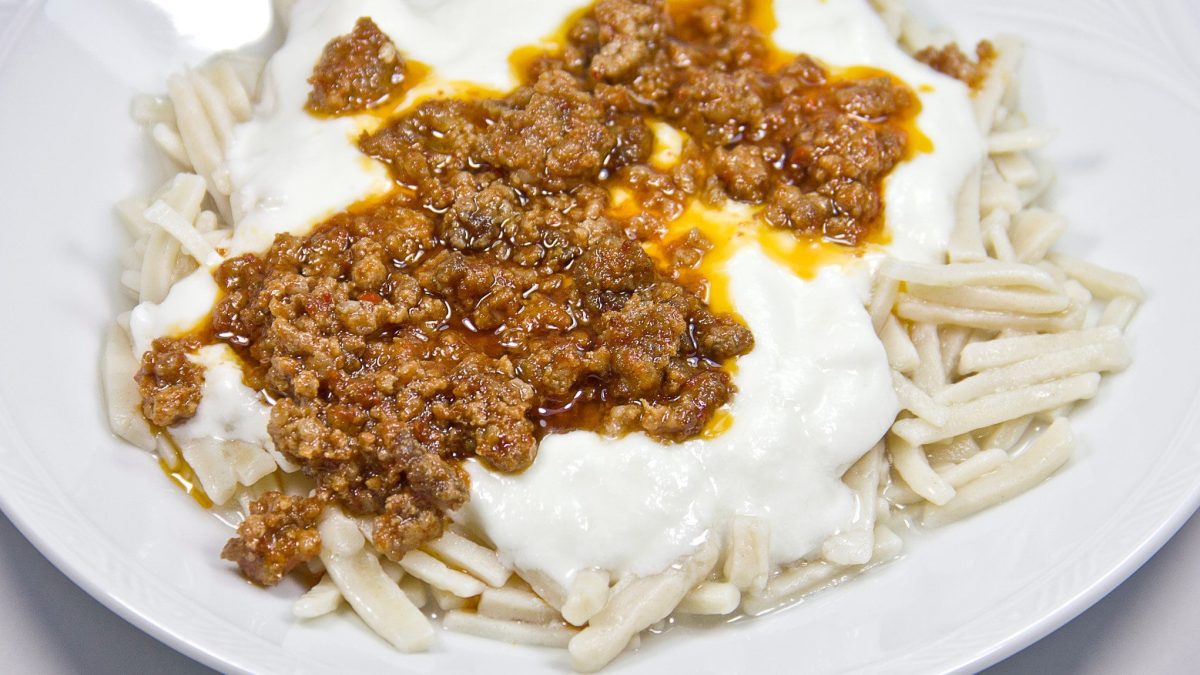 Kiymali Yogurtlu Eriste auf weißem Teller vor hellem Hintergrund. Draufsicht.