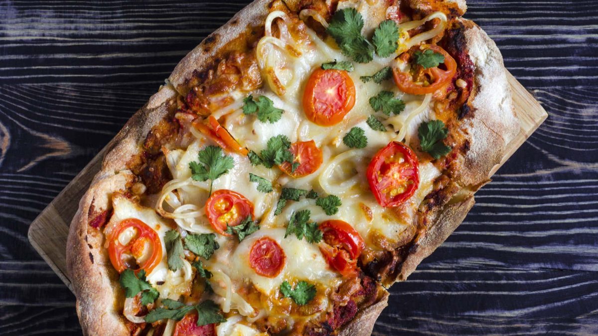Ein vegetarisch belegtes Stück Pinsa auf Holzbrett.