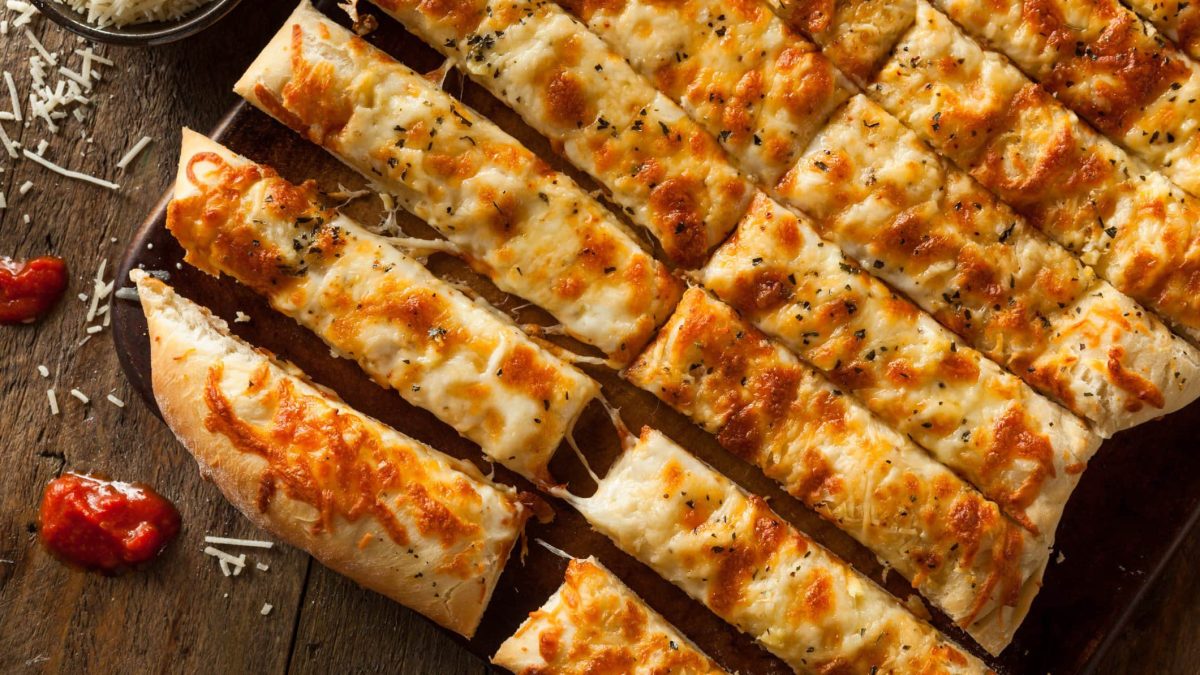 In Streifen geschnittene Pizzastangen mit Käse auf Holzuntergrund.