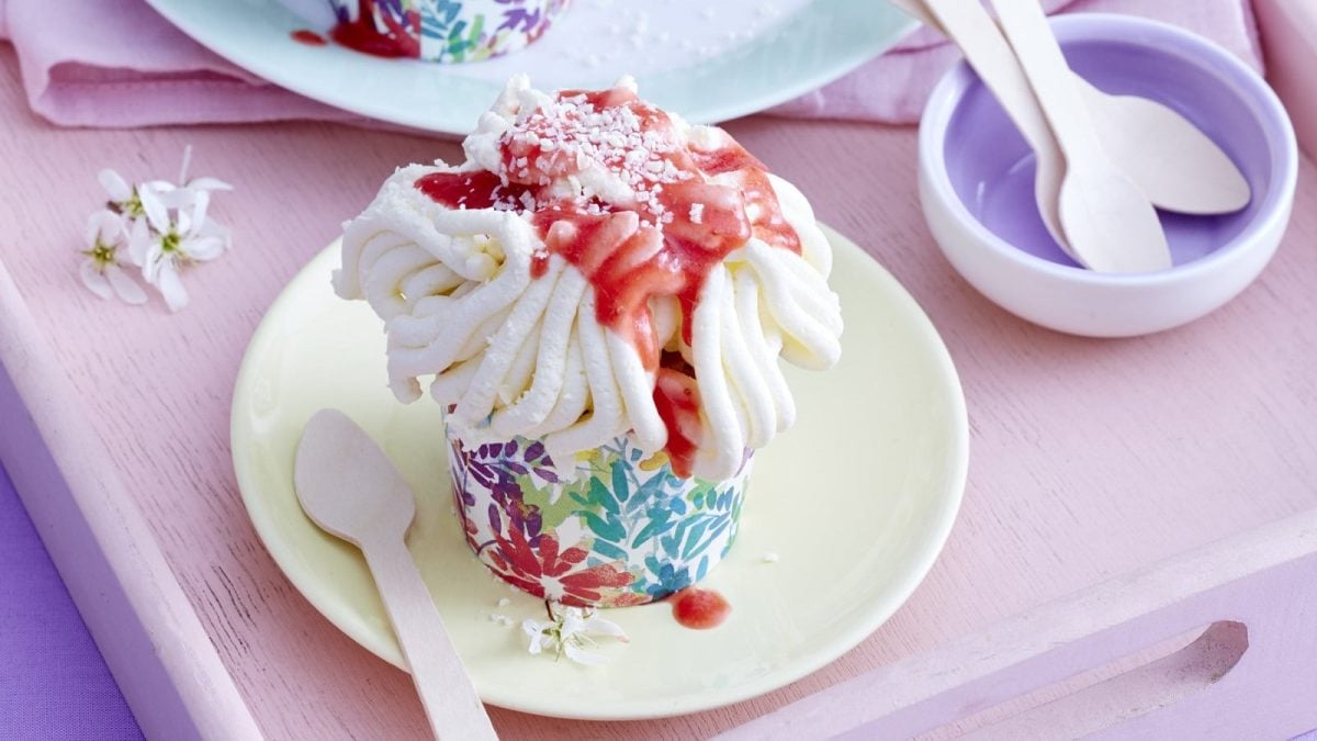 Auf einem kleinen Teller steht eine Portion der Spaghettieis-Cupcakes. Er ist mit Erdbeersauce und weißer Schokolade verziert.