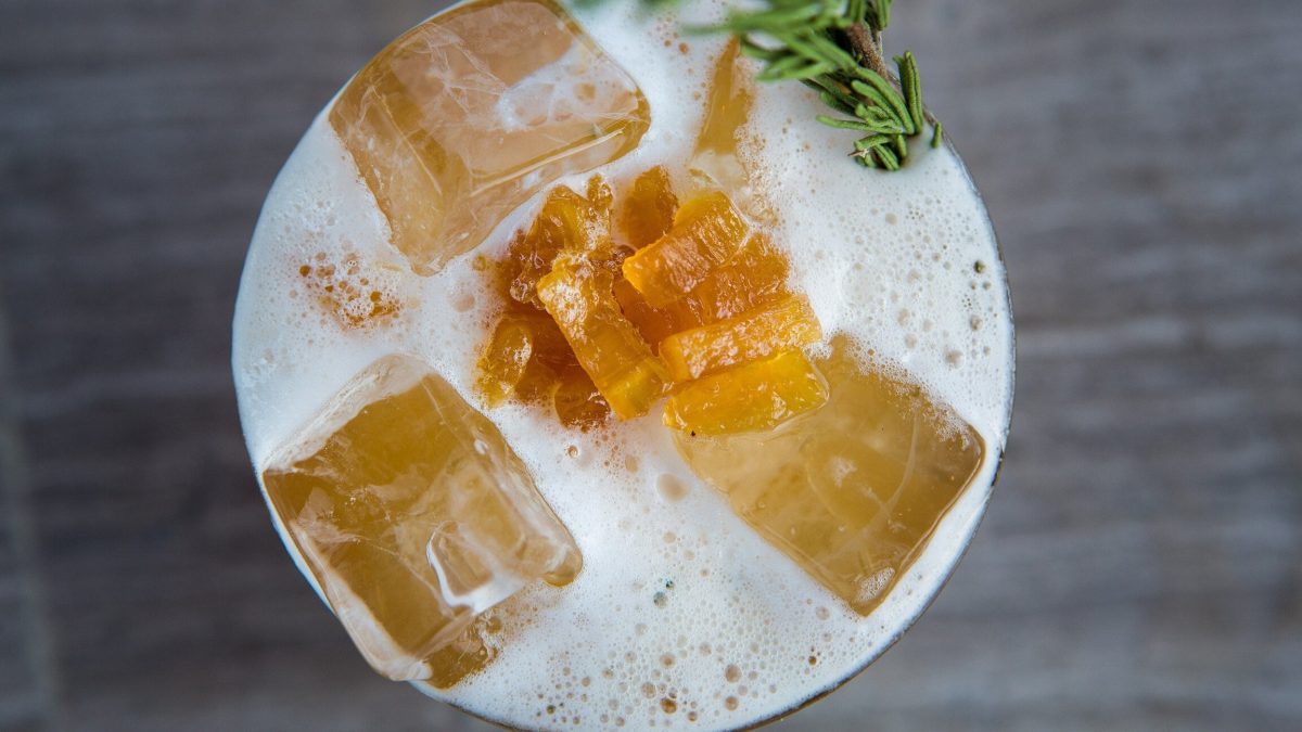 Beer Gin Fizz mit kandiertem Ingwer und Rosmarin auf grauem Tisch. Draufsicht.