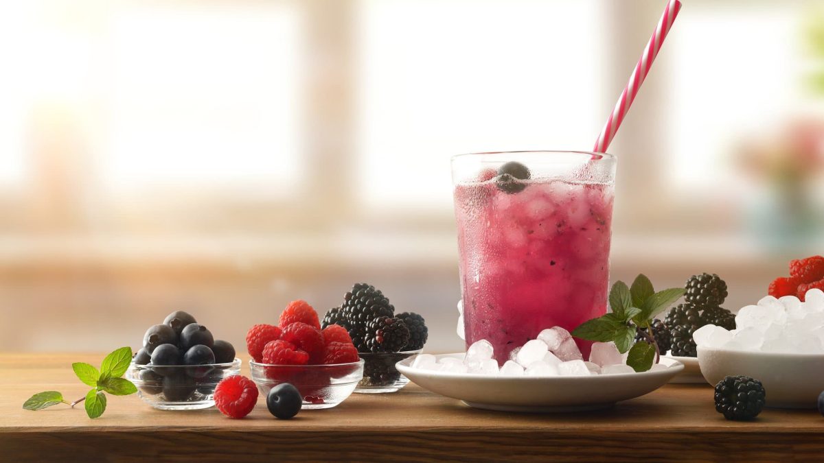 Berries on the Rocks auf Holzbrett mit Beeren und Eiswürfeln und Minzblättern. Frontalaufnahme.