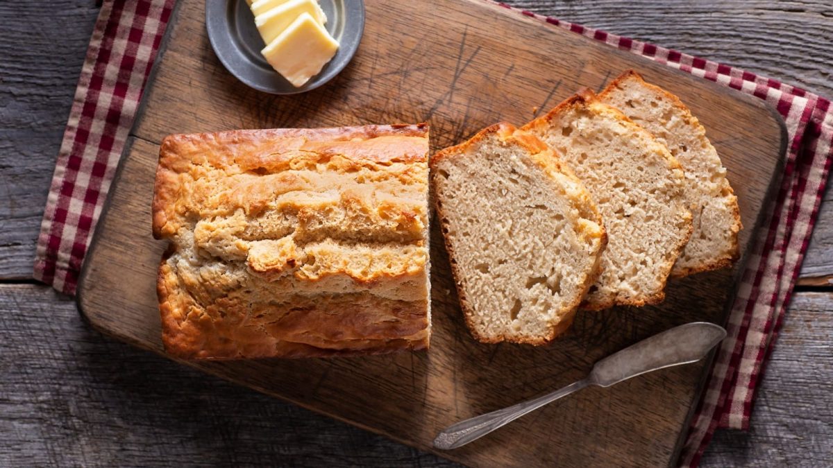 Bierbrot in Kastenform auf einem Holzbrett neben Butter