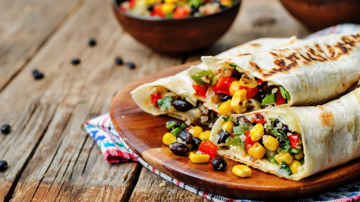 Ein Brett mit drei Breakfast Burritos, die mit Mais, Bohnen, Salat, Paprika und mehr gefüllt sind.