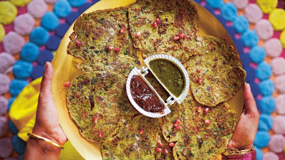 Draufsicht: Die Hände einer Frau halten einen Teller mit Chila, Mungobohnenfladen aus Indien, in der Mitte steht eine Schale mit zwei Dips.