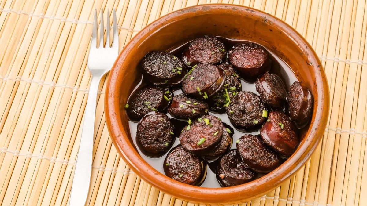 Chorizo in Rotwein in Tapasschale auf Bambusmatte. Daneben Gabel. Draufsicht.