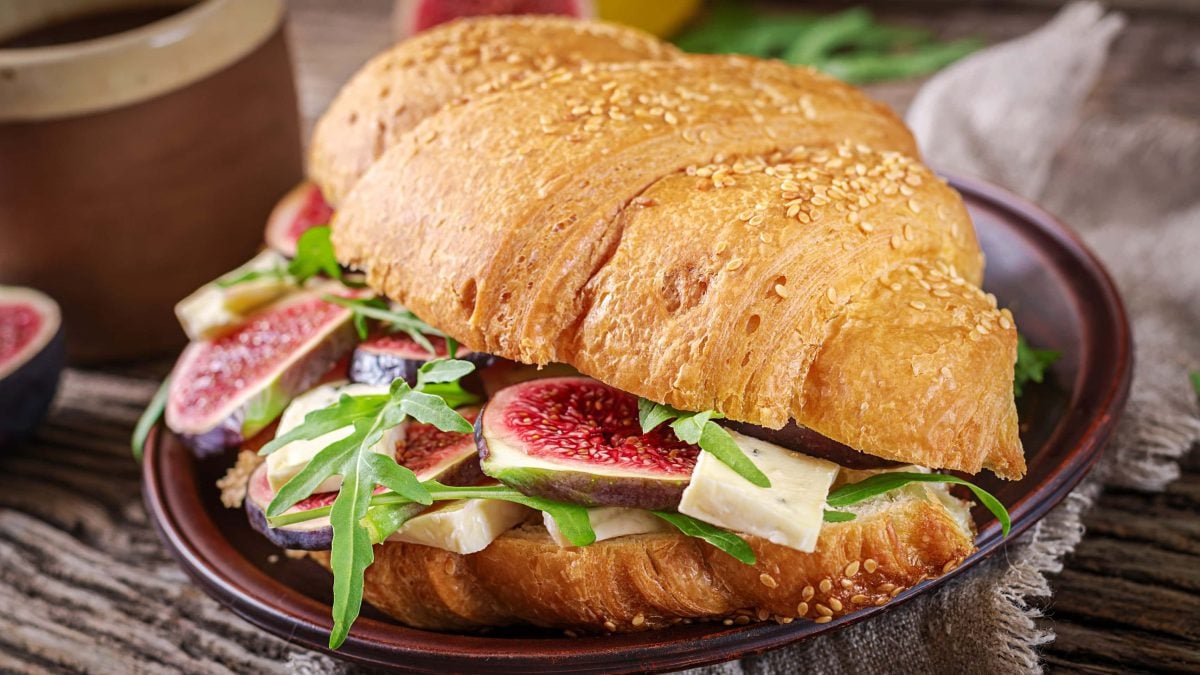 Ein aufgeschnittenes Croissant mit Brie und Feigen auf einem dunklem Teller und Holzuntergrund.
