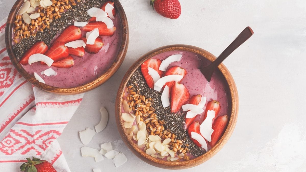 Zwei Schalen Erdbeer-Smoothie-Bowl mit Erdbeeren, Kokoschips, Mandelblätten, in der Draufsicht.