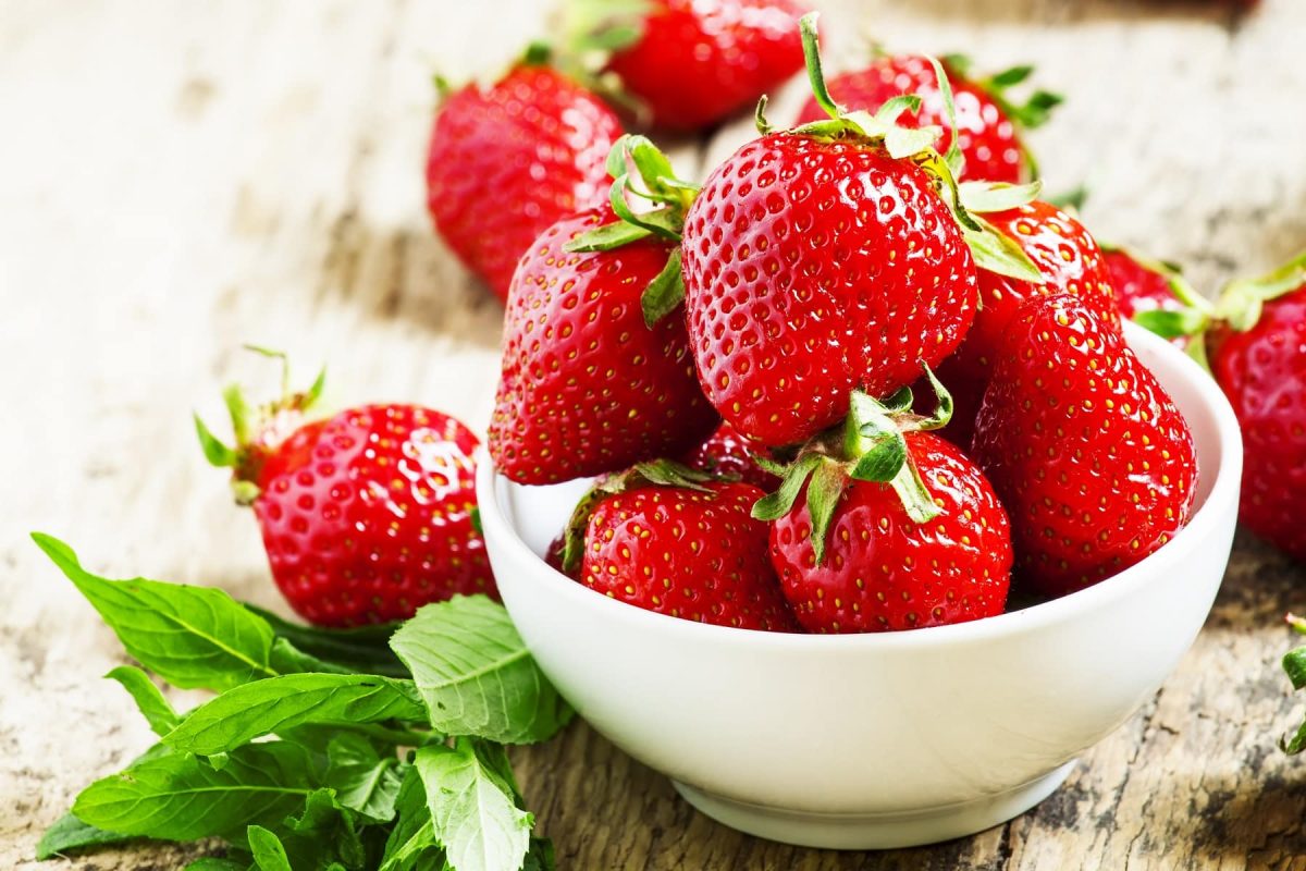 Frische Erdbeeren in einer weißen Schüssel auf einem Untergrund aus Holz. Und so wurden sie länger frisch halten.