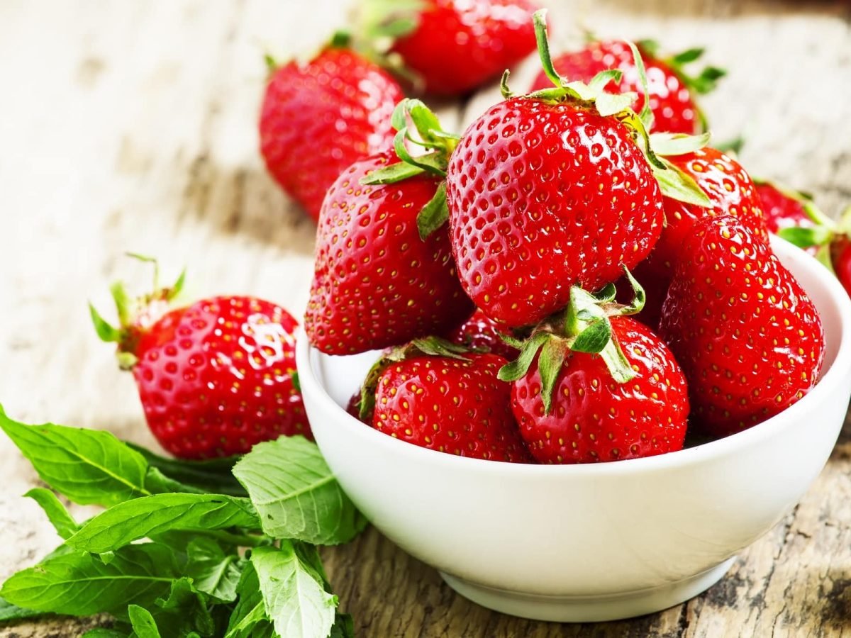 Frische Erdbeeren in einer weißen Schüssel auf einem Untergrund aus Holz. Und so wurden sie länger frisch halten.