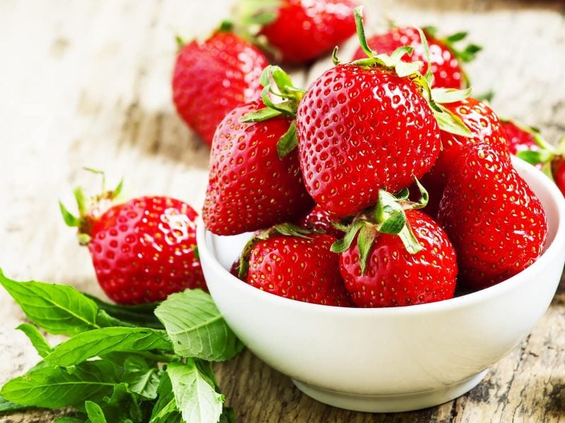 Frische Erdbeeren in einer weißen Schüssel auf einem Untergrund aus Holz. Und so wurden sie länger frisch halten.