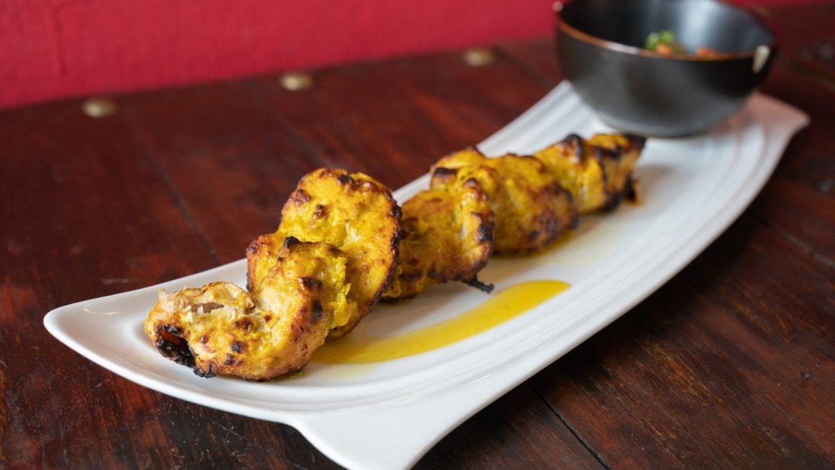 Gegrillte Hähnchenbrust in Zitronen-Knoblauch-Marinade auf weißem Teller und dunklem Untergrund. Daneben Schale mit Curry-Sauce. Frontalansicht.