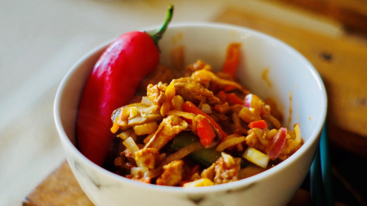 Hackpfanne mit Reis und Halloumi in weißer Schale mit ganzer Chilischote auf Holzbrett. Draufsicht.