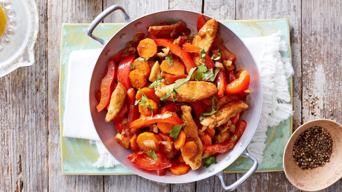 Hähnchen-Wok mit Paprika, Koriander und Möhren in der Pfanne vor hellem Hintergrund.