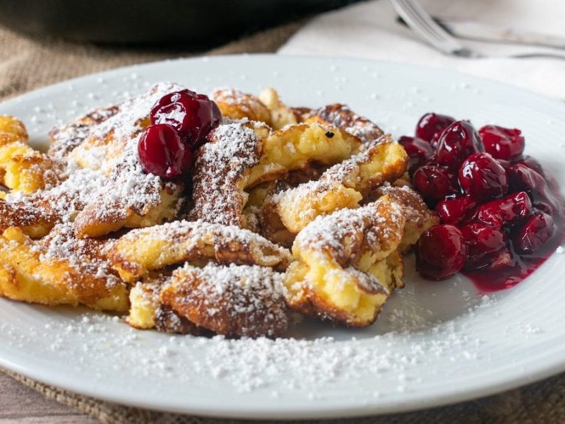 Ein Kaiserschmarrn mit Kirschen liegt auf einem weißen Teller.