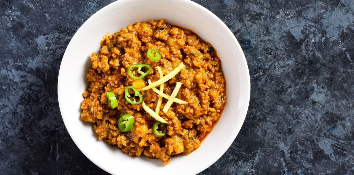 Ein weißer Teller mit dem Keema Curry auf einem blau-marmorierten Tisch.
