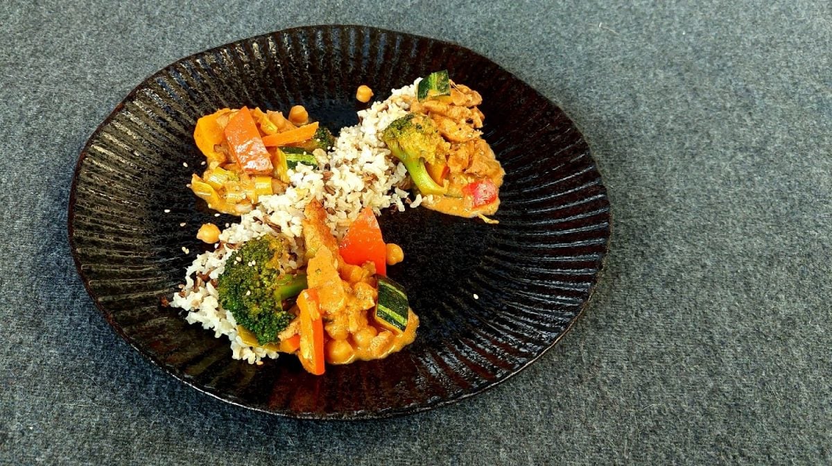 Ein schwarzer Teller mit Wildreis und dem roten Kürbis-Curry auf einem dunkelgrauen Untergrund.