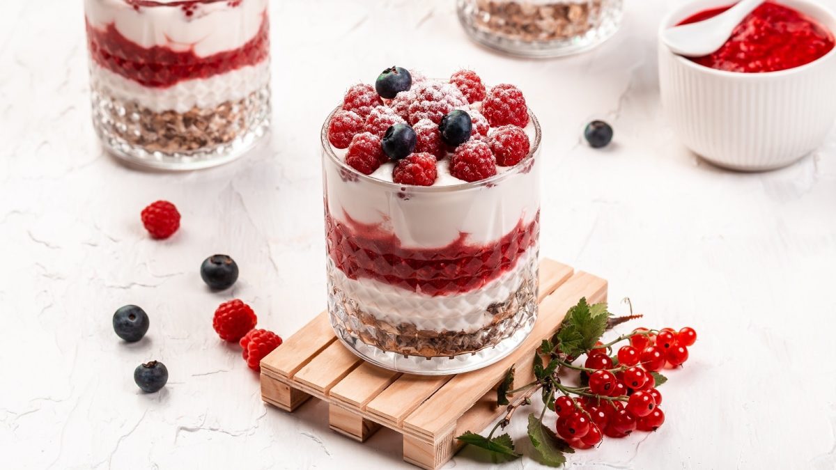Ein Glas mit Himbeer-Cheesecake im Glas neben frischen Beeren