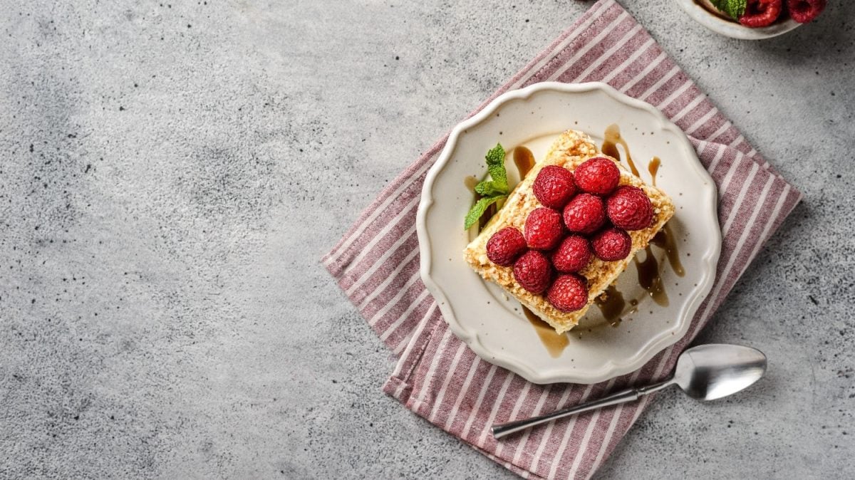 Ein Stück Napoleon-Torte auf einem weißen Teller mit einer rot-weiß-gestreiften Tischdecke auf einem grauen Tisch.