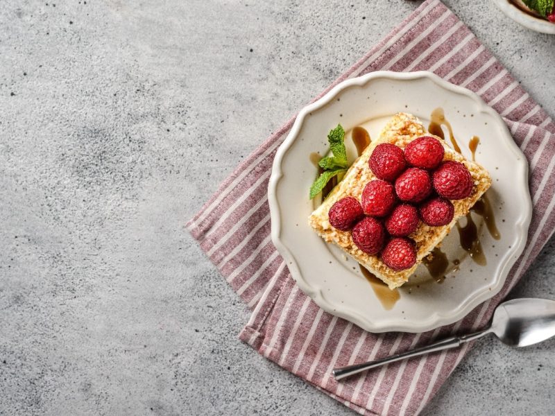 Ein Stück Napoleon-Torte auf einem weißen Teller mit einer rot-weiß-gestreiften Tischdecke auf einem grauen Tisch.