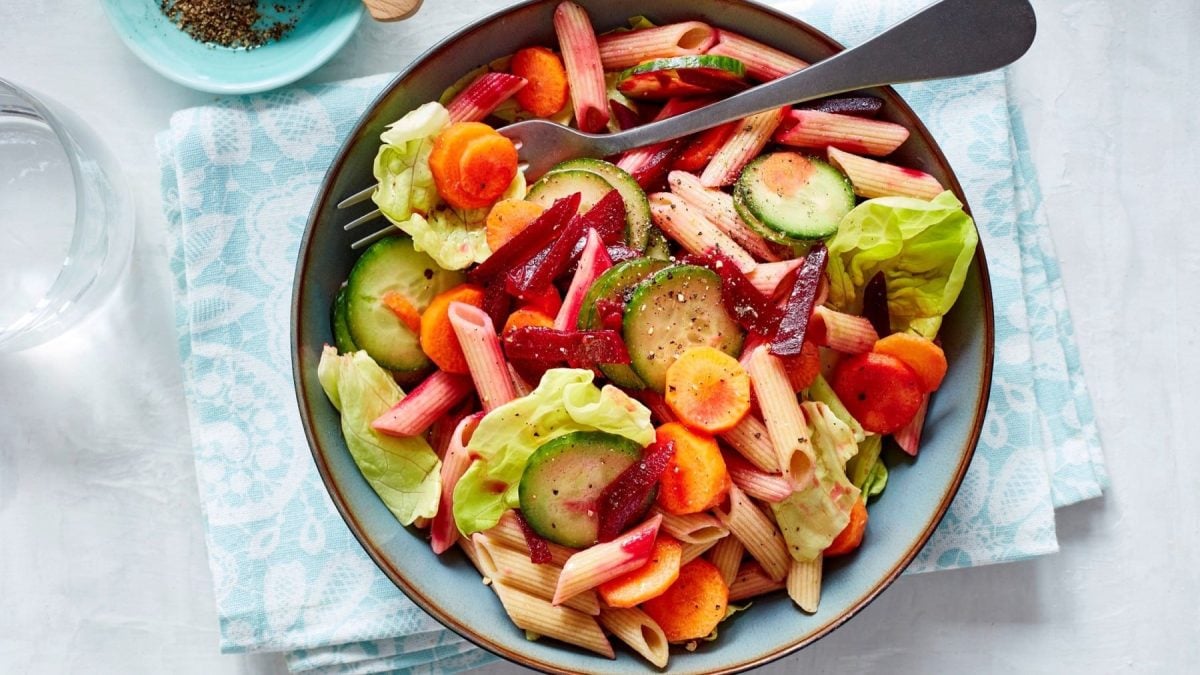 Nudelsalat mit Rote Bete in einer blauen Schüssel auf einem blauweißen Küchentuch.