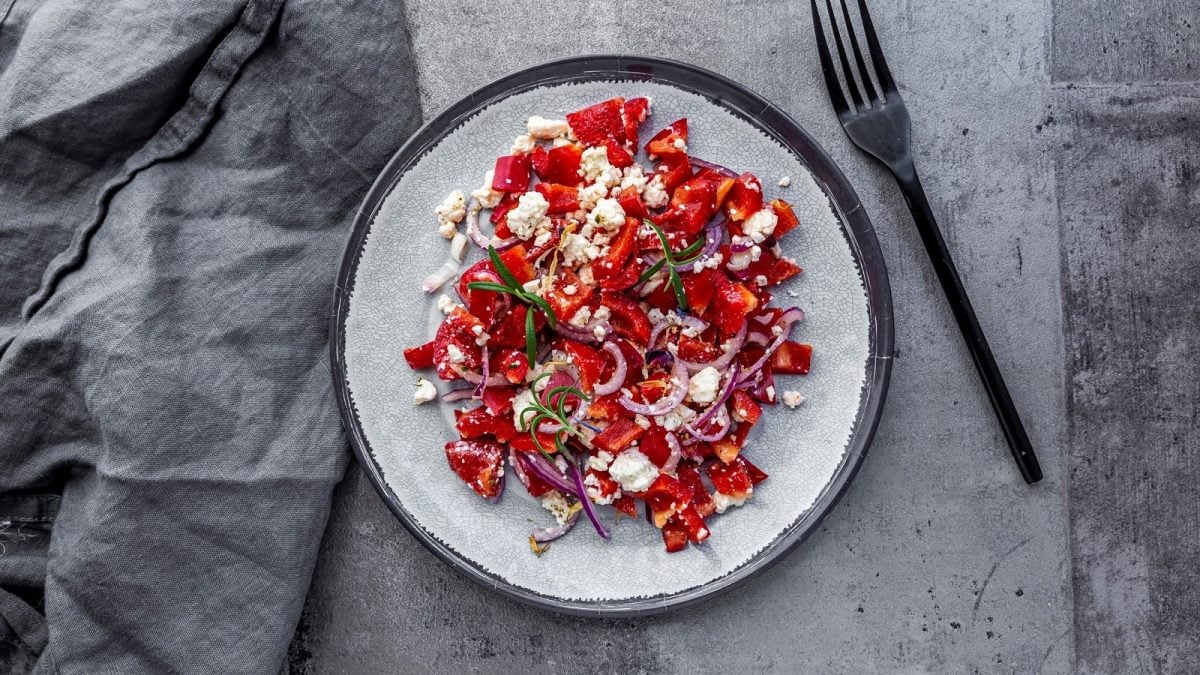 Ein weißer Teller auf grauem Untergrund mit Paprika-Salat mit Feta