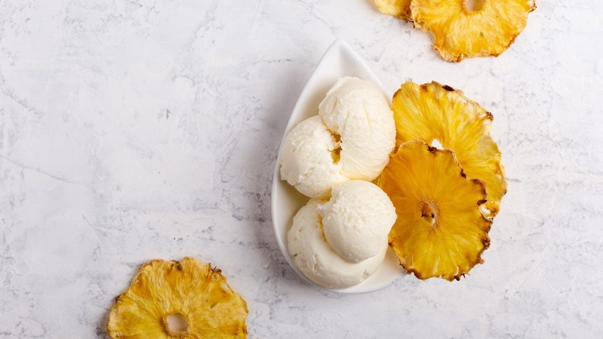Eine Schale Piña Colada Nicecream, daneben liegen getrocknete Ananasscheiben, alles Draufsicht.