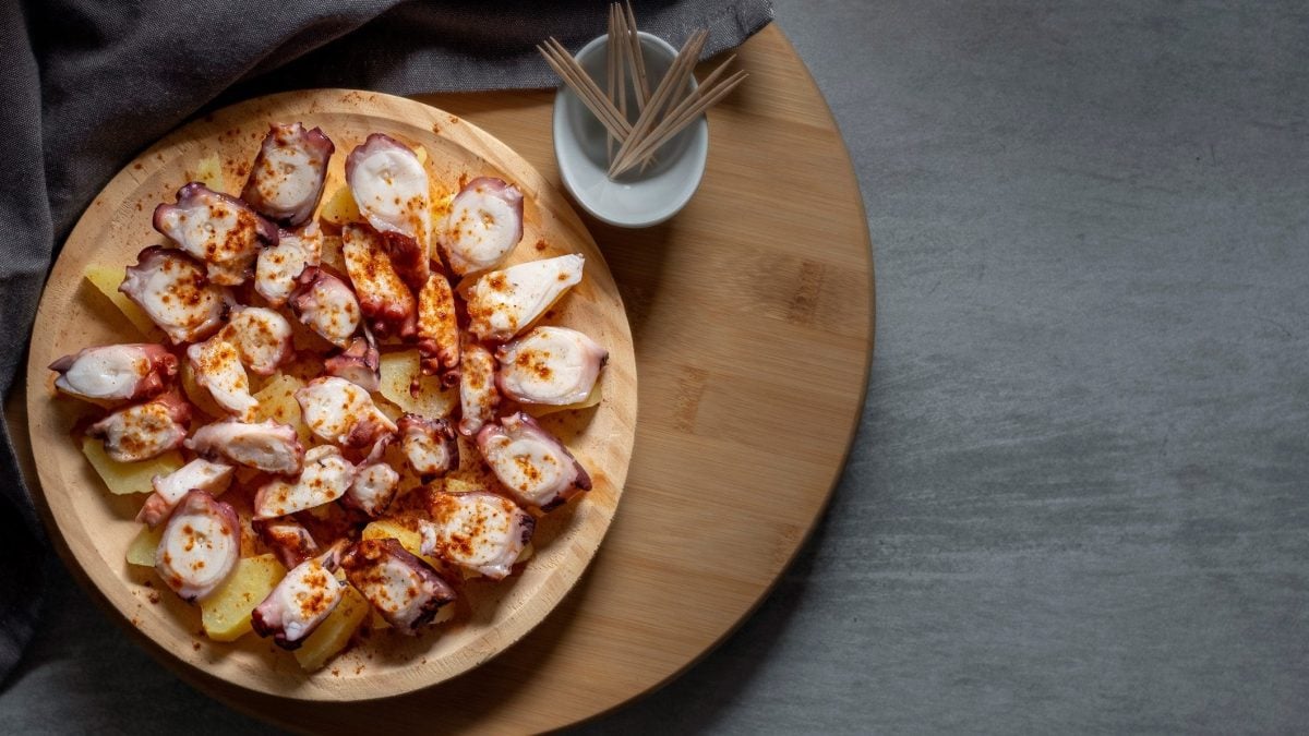 Pulpo a feira mit Kartoffeln auf Holzbrett. Daneben Zahnstocher. Draufsicht.