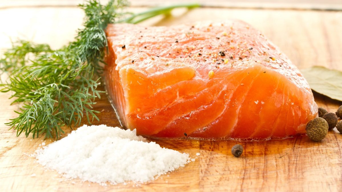 Selbst gebeizter Lachs mit Salt, Pfeffer und Dill auf Holzbrett. Frontalansicht.