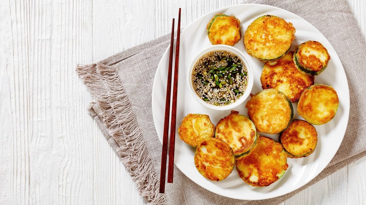 Ein weißer Teller mit Hobak Jeon auf einem braunen Geschirrtuch.
